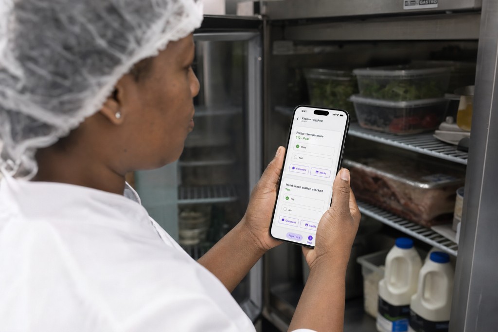 Steward completing a kitchen hygiene check on a phone beside an open fridge