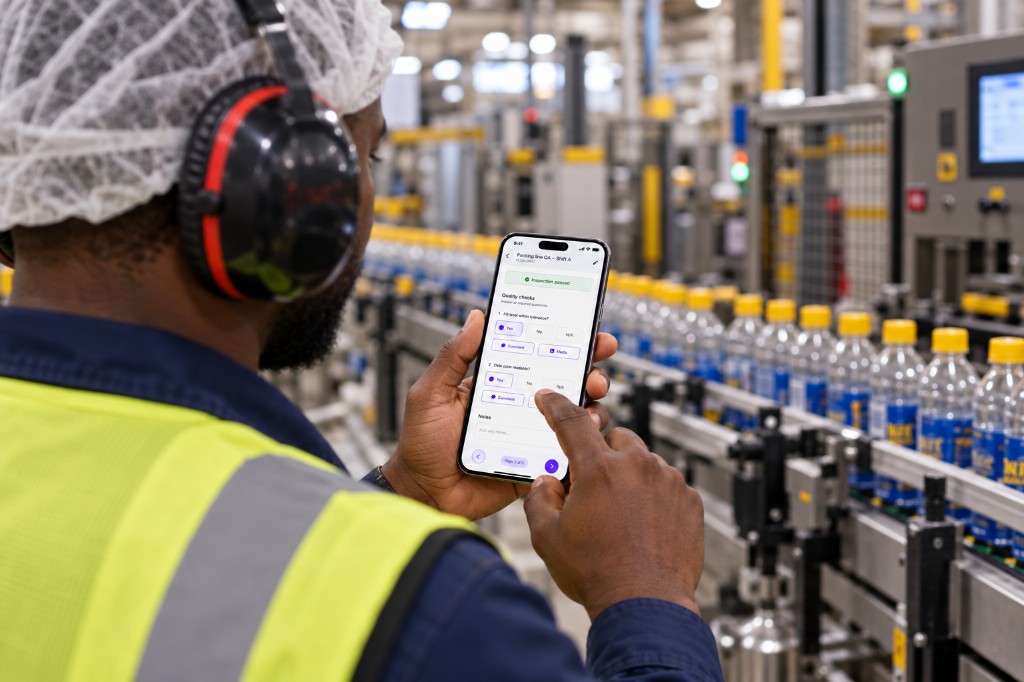 Operator completing a packing-line quality check on a phone beside the bottling line